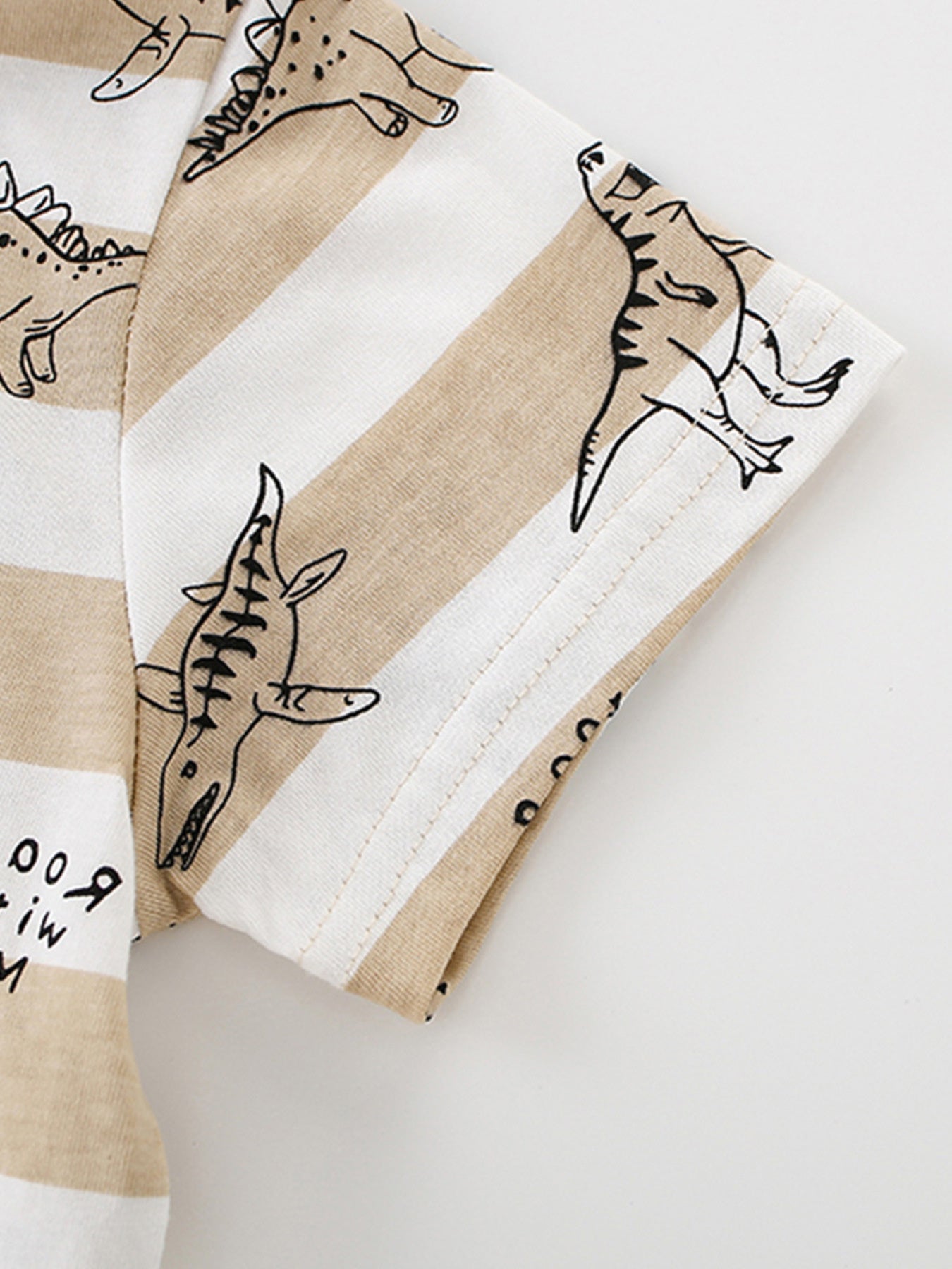 Close-up of the short sleeve hem and dinosaur print on a tan and white striped children's T-shirt