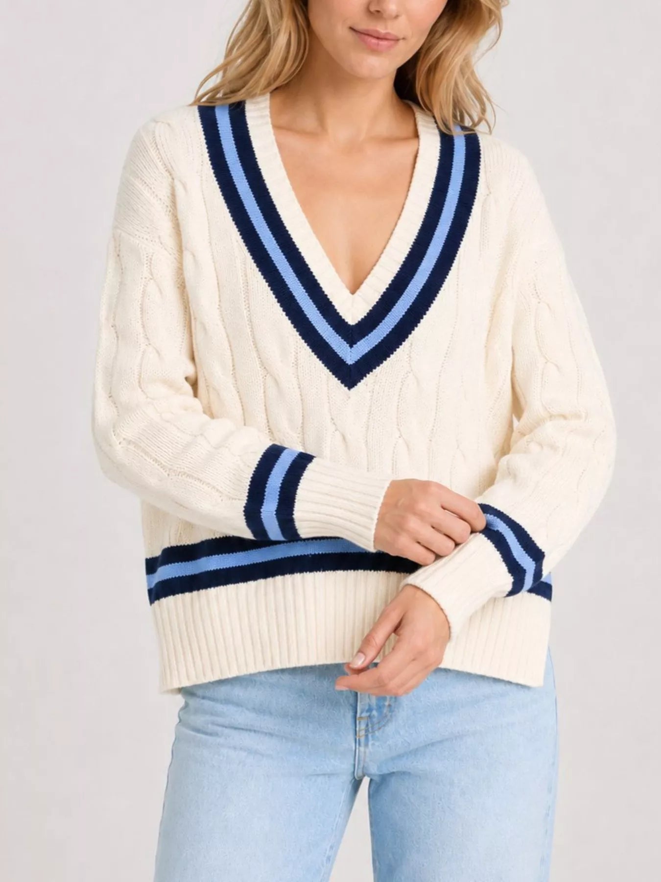 On-model front view of a cream cable knit sweater with striped cuffs, arms crossed