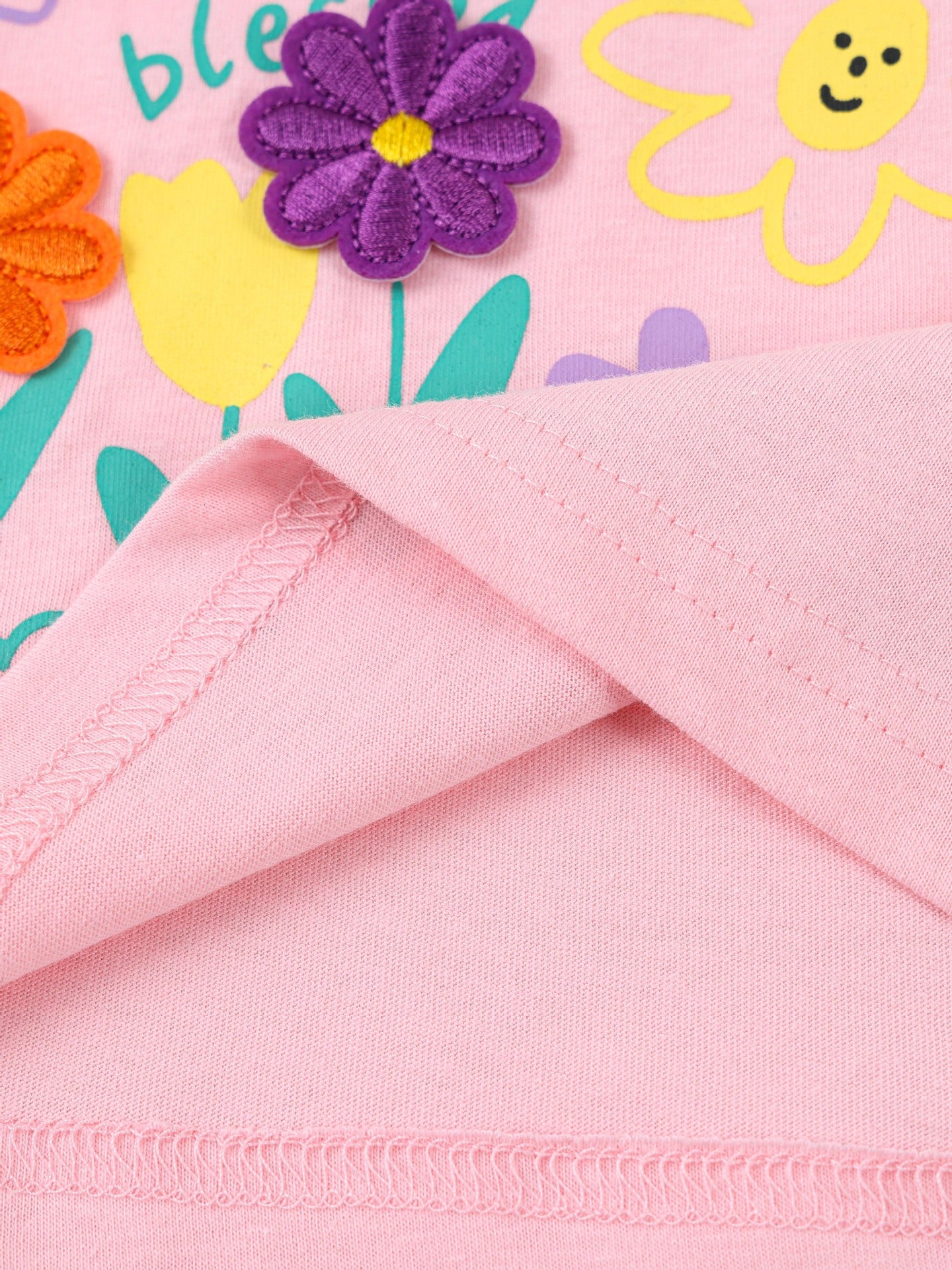 Close-up of pink children's t-shirt hem stitching with purple flower applique and printed flowers above