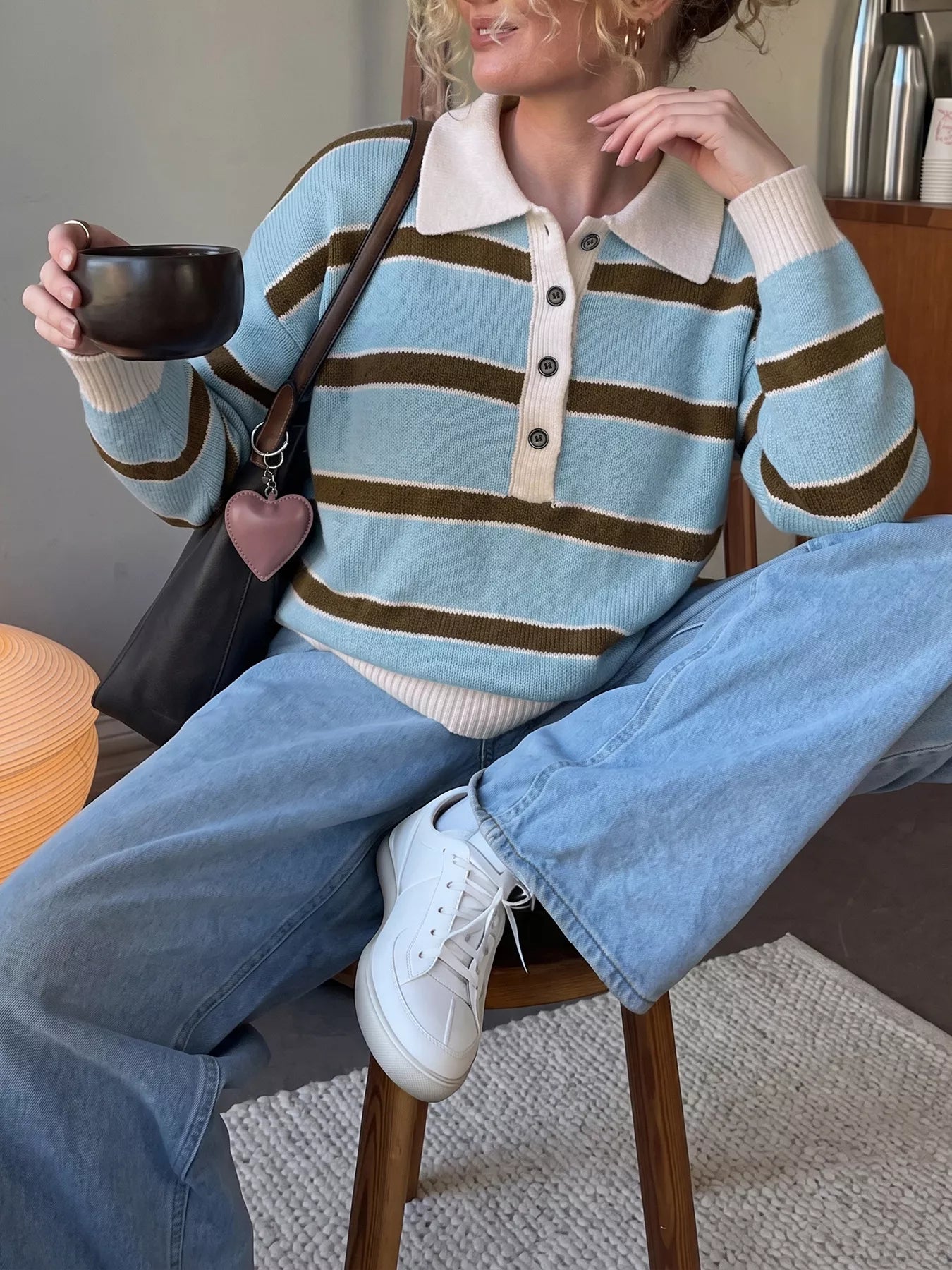 Seated front view of blue and brown striped polo sweater worn with light jeans.