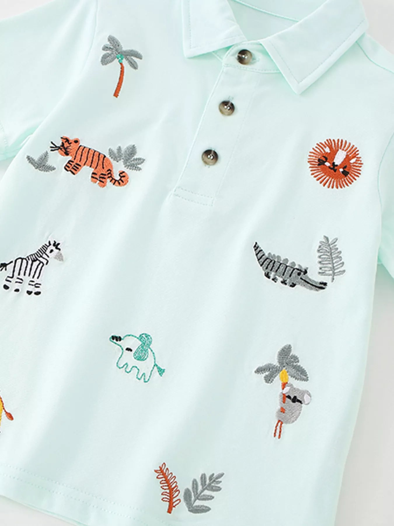 Angled front view of the mint blue polo showing embroidered tiger, lion, crocodile and koala motifs