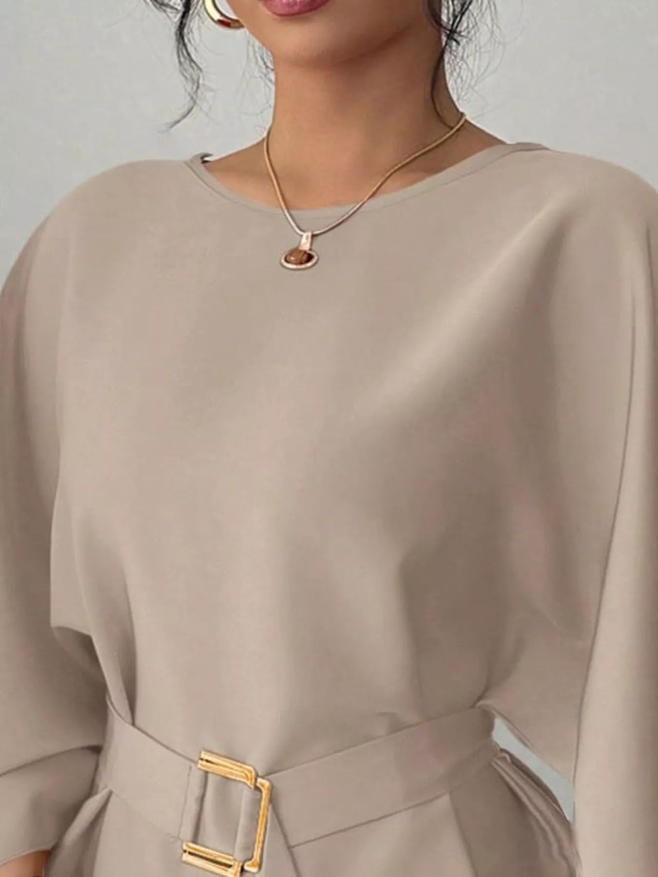 Close view of khaki round neck blouse showing neckline and gold buckle belt