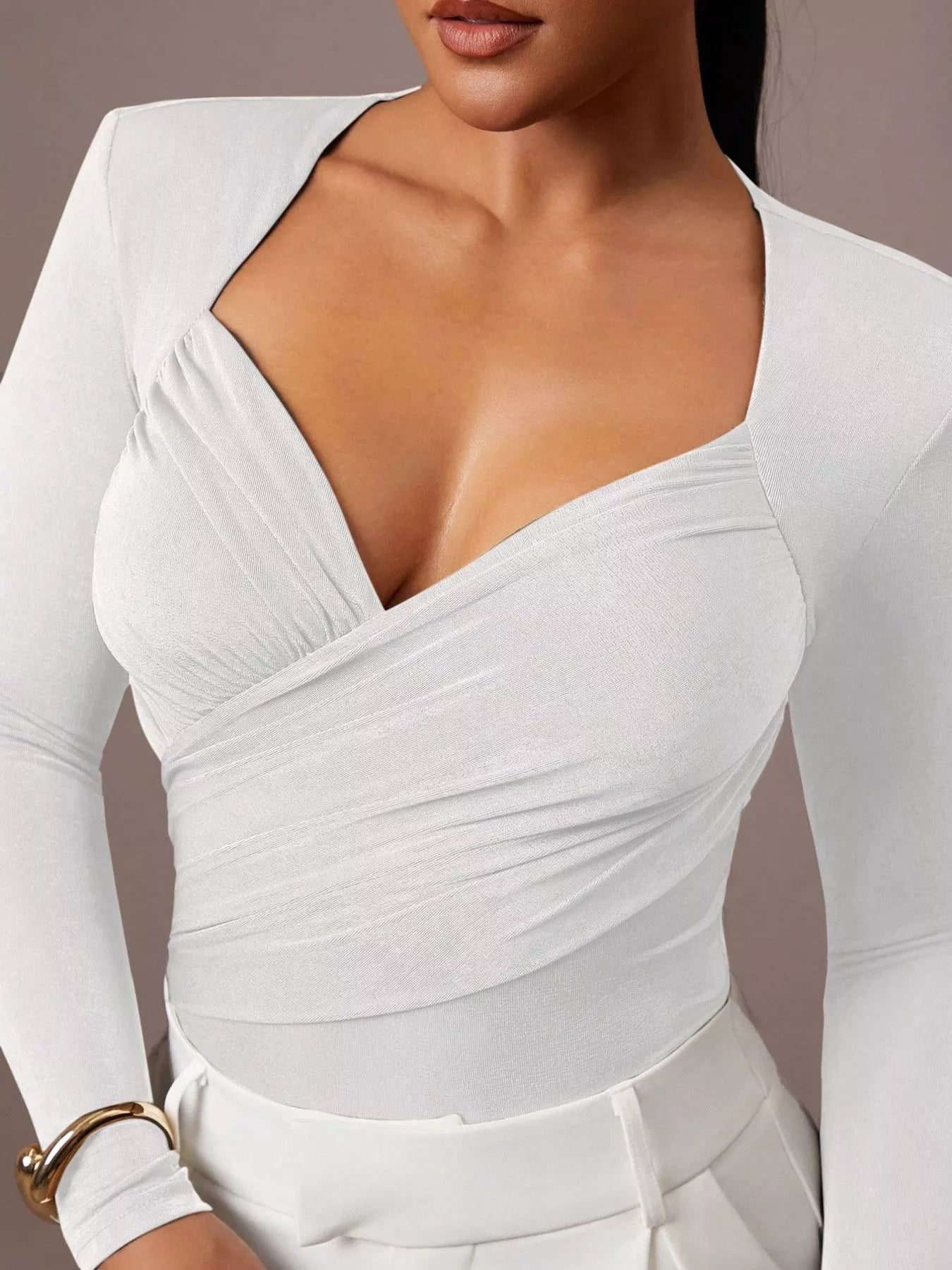 Close cropped front view of white ruched surplice bodysuit paired with white trousers