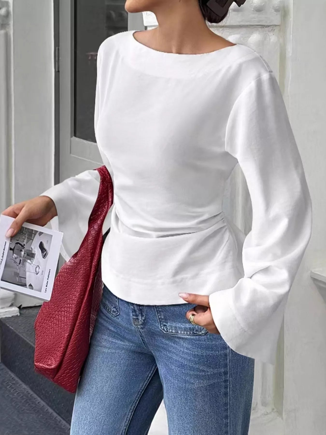 Angled front view of white boat neck long sleeve slim fit top holding a magazine outdoors