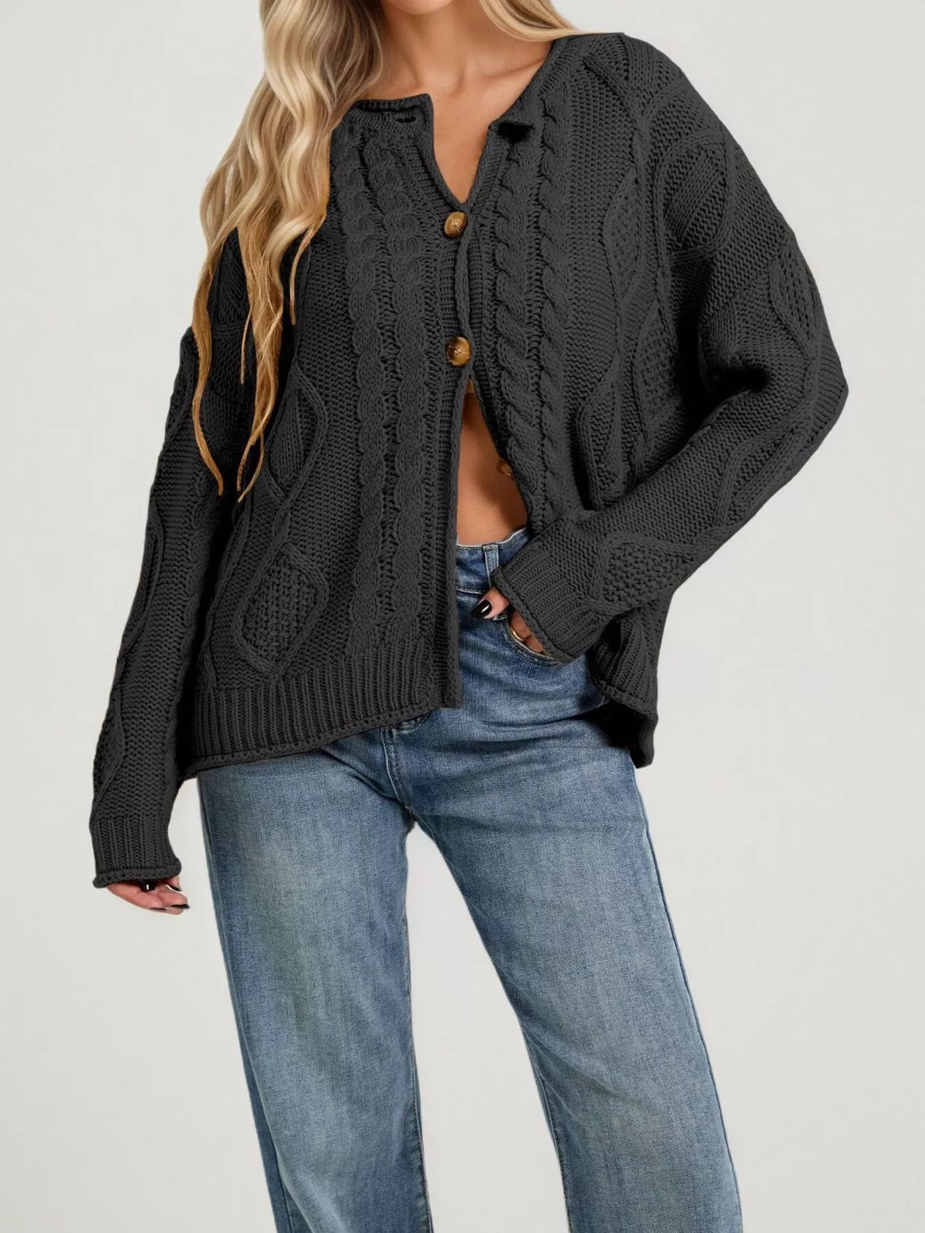 Front view of black cable knit button down cardigan with brown buttons and blue jeans