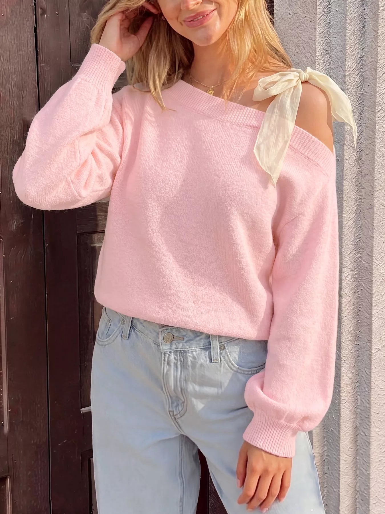 Front view of a pink one-shoulder sweater with a cream bow and long balloon sleeves