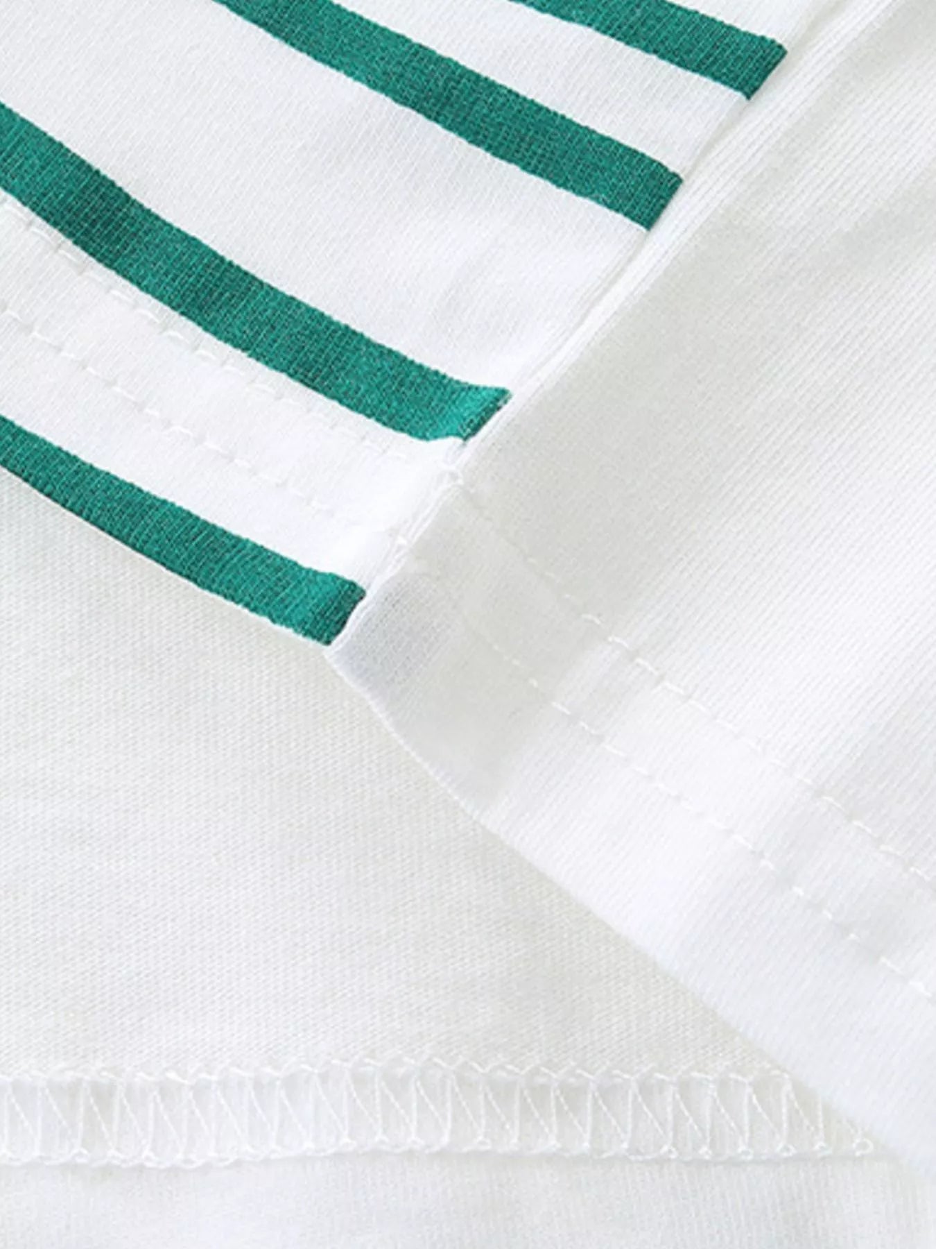 Close-up of white t-shirt hem stitching beside green and white striped fabric panel