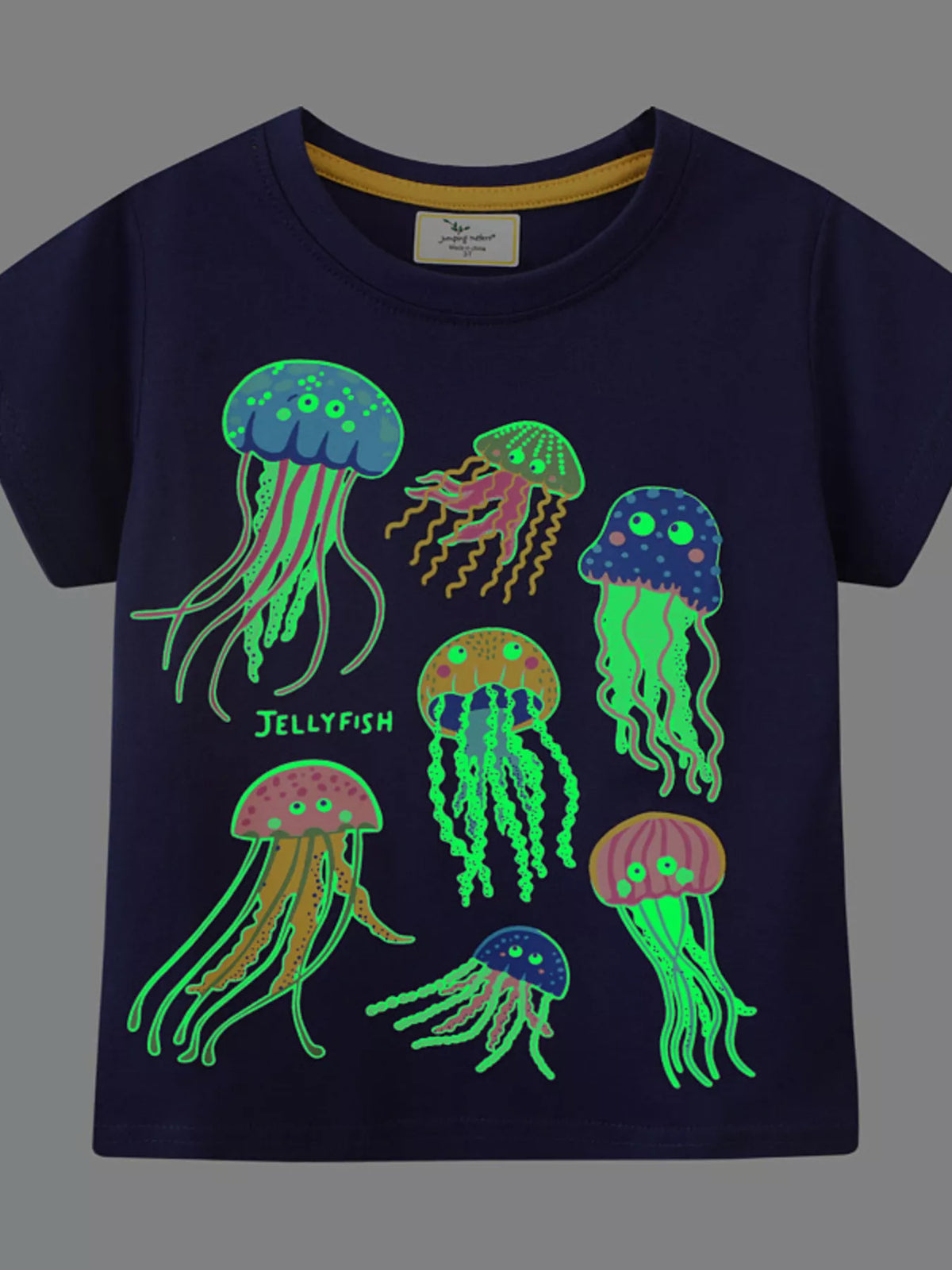 Front view of black children's tee in the dark with glowing green jellyfish graphic