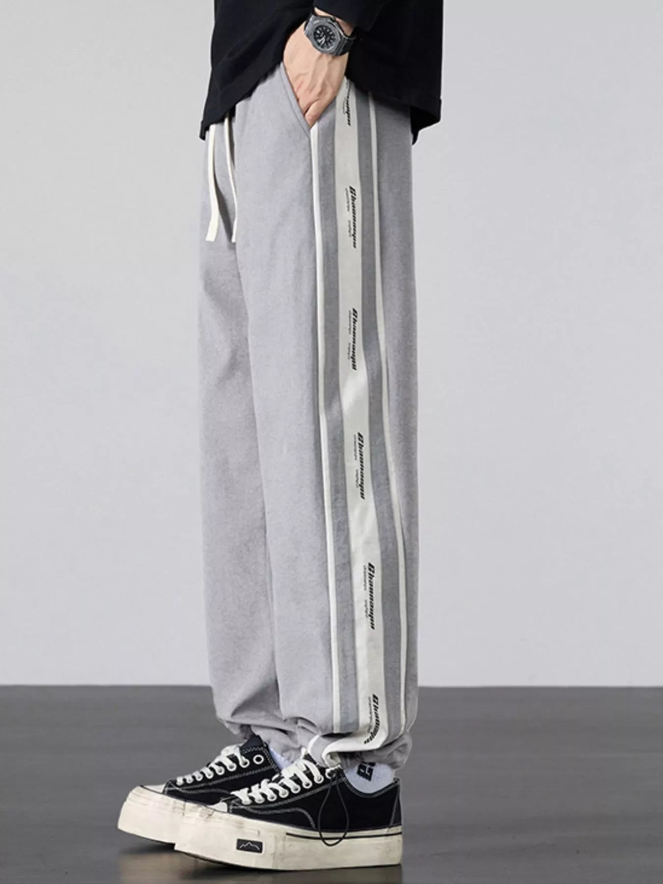 Men's gray loose-fit pants with side stripes and a drawstring waist.