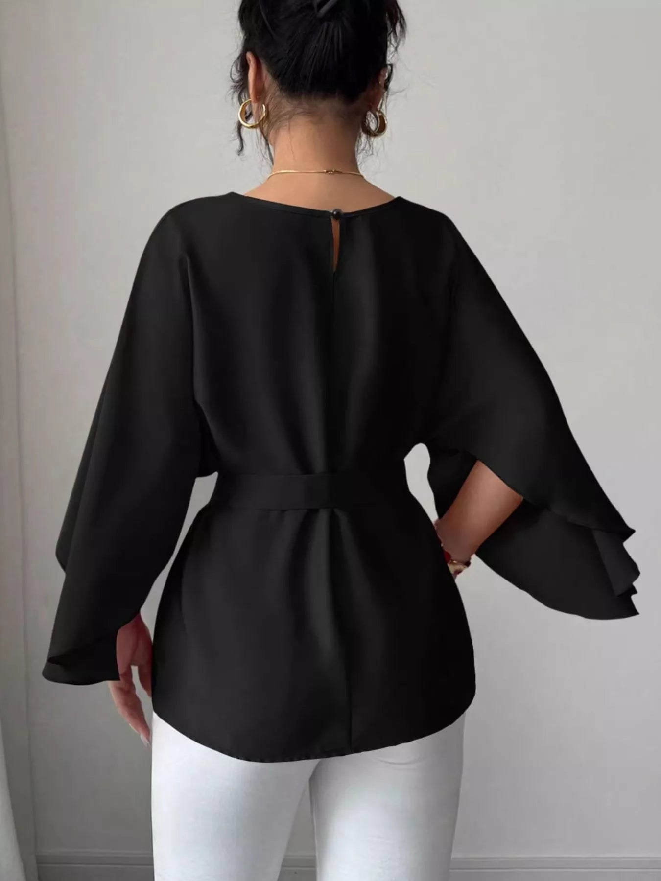 Back view of black batwing sleeve blouse showing button keyhole neckline and belted waist